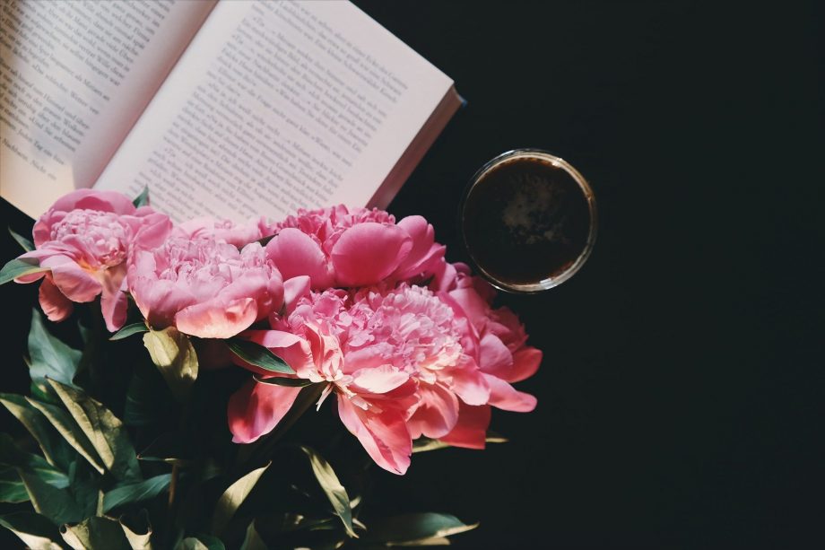pink flowers lying across open book next to cup of coffee